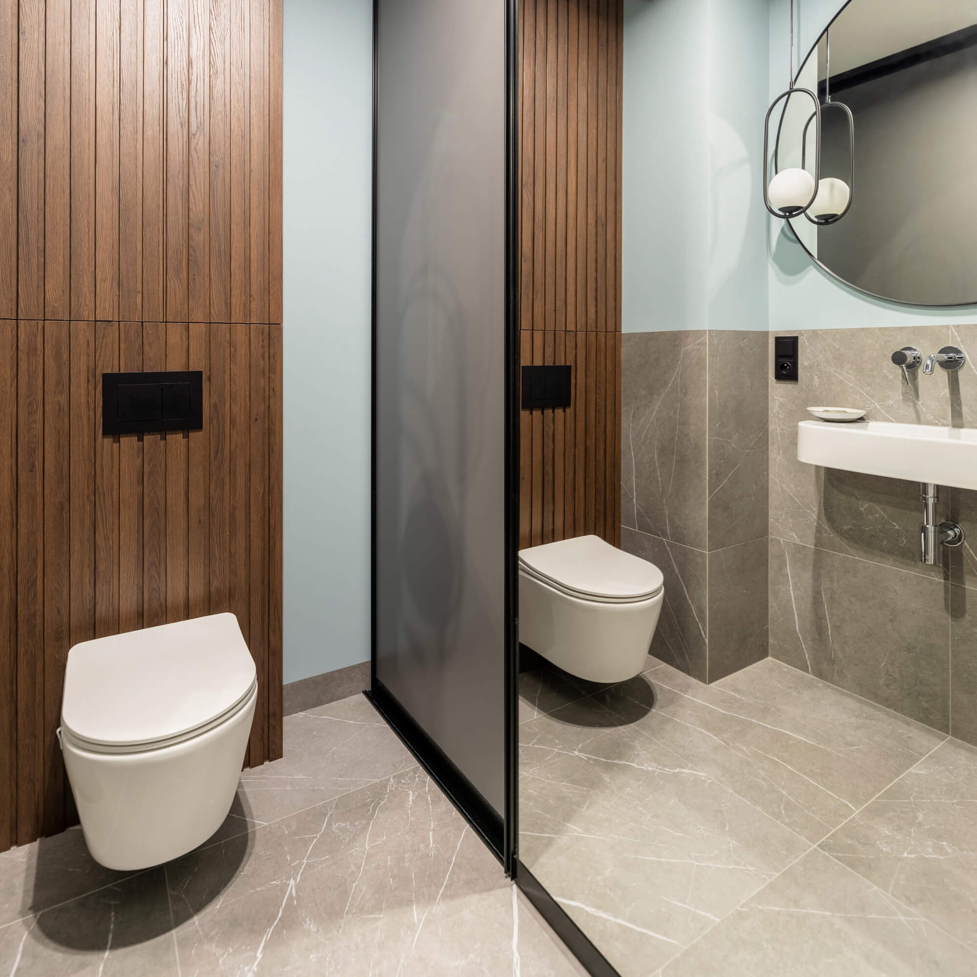 Designat badrum med träpanel, frostat glas och två vägghängda toaletter – stilren badrumsrenovering.