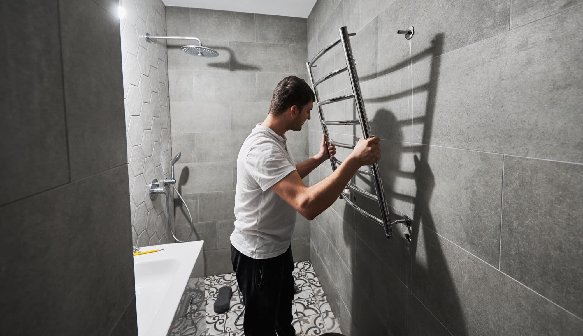 Hantverkare monterar en kromad handdukstork på kaklad vägg under badrumsrenovering.
