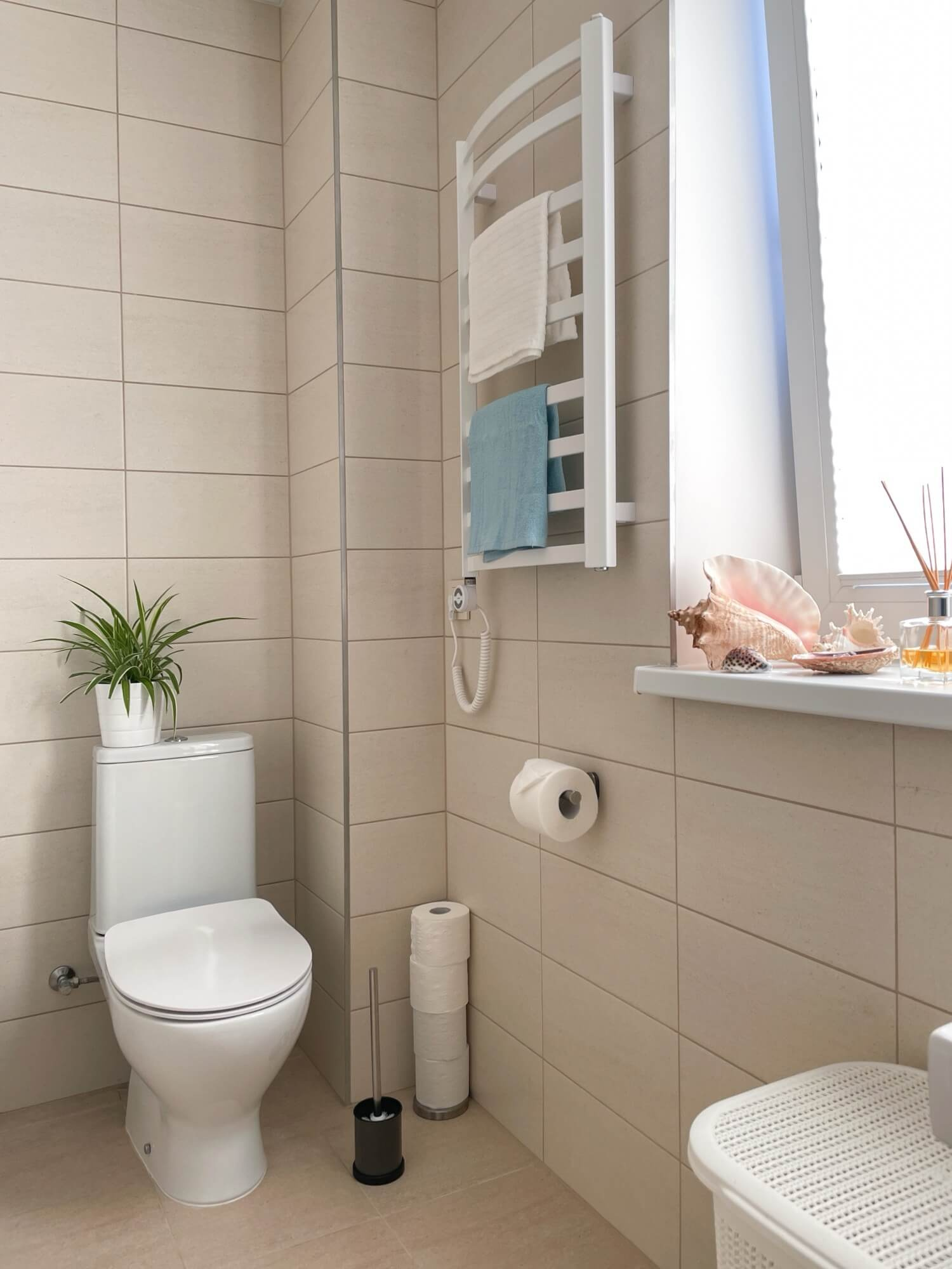 Ljust kaklat badrum med wc och elhanddukstork vid fönster, typisk lösning i badrumsrenovering.