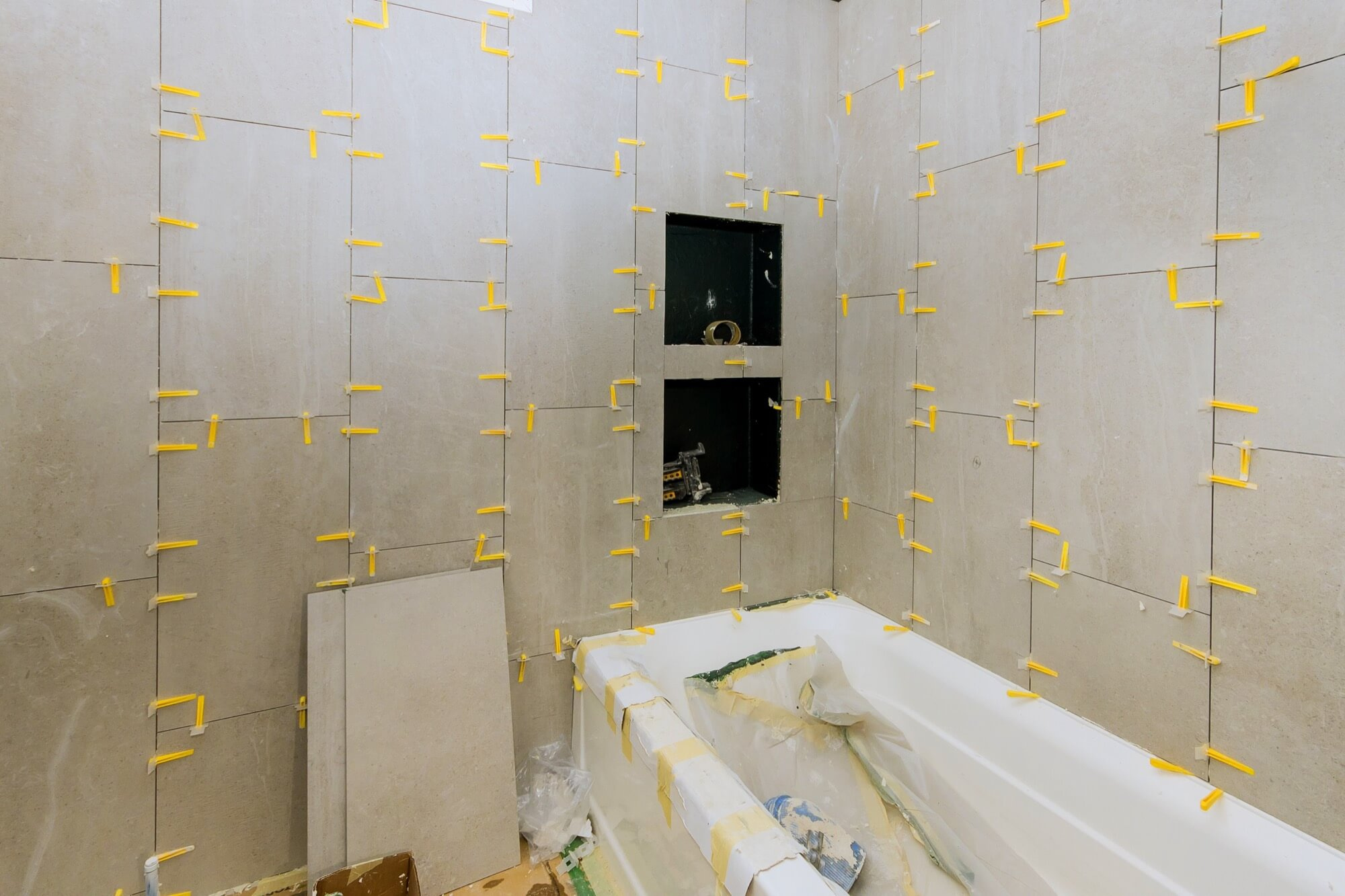 Pågående badrumsrenovering med stora väggplattor som monteras med nivåclips runt ett inbyggt badkar.